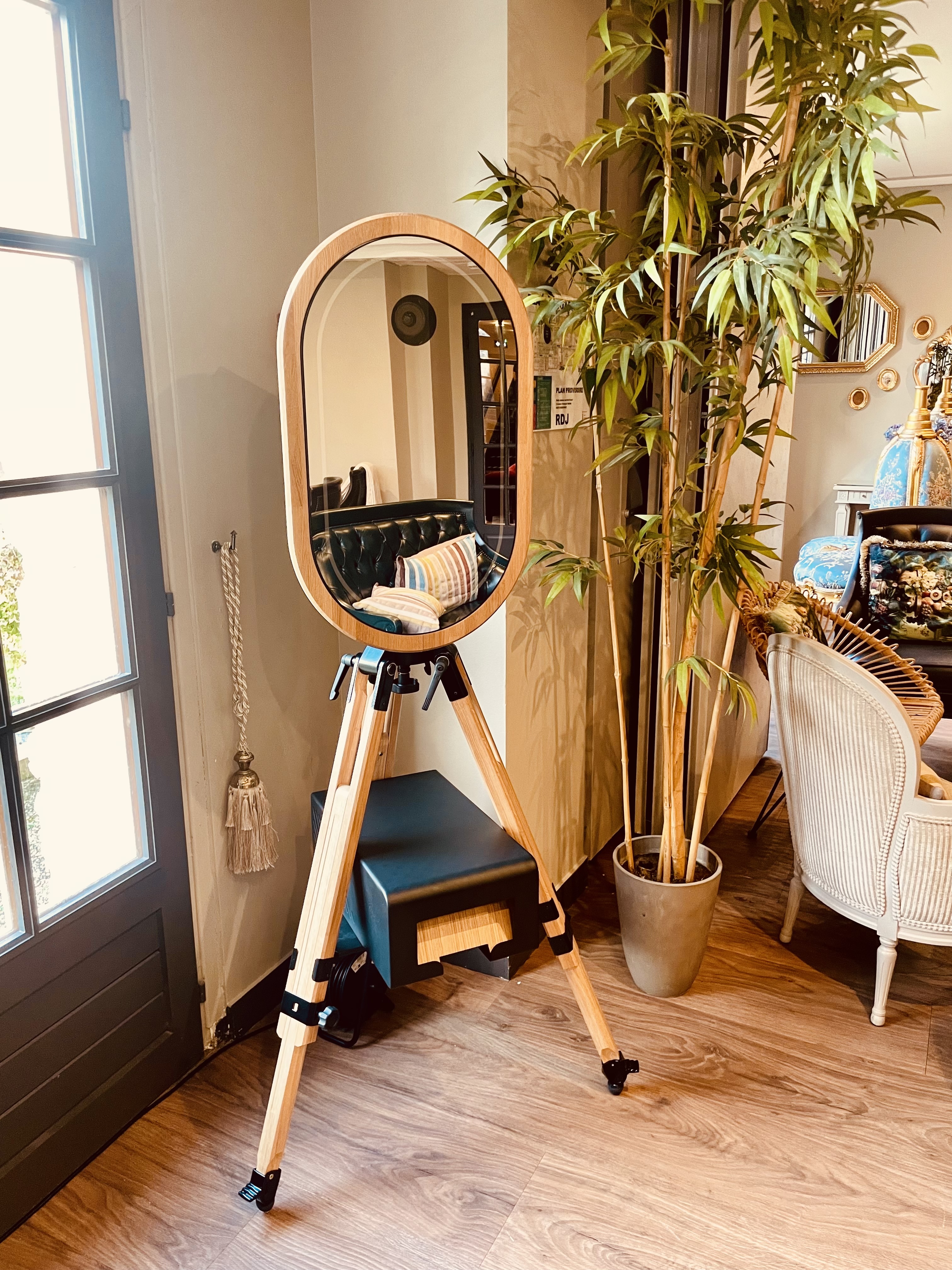 Photobooth miroir MODJA sur pied trépied en bois, installé dans un intérieur chaleureux.