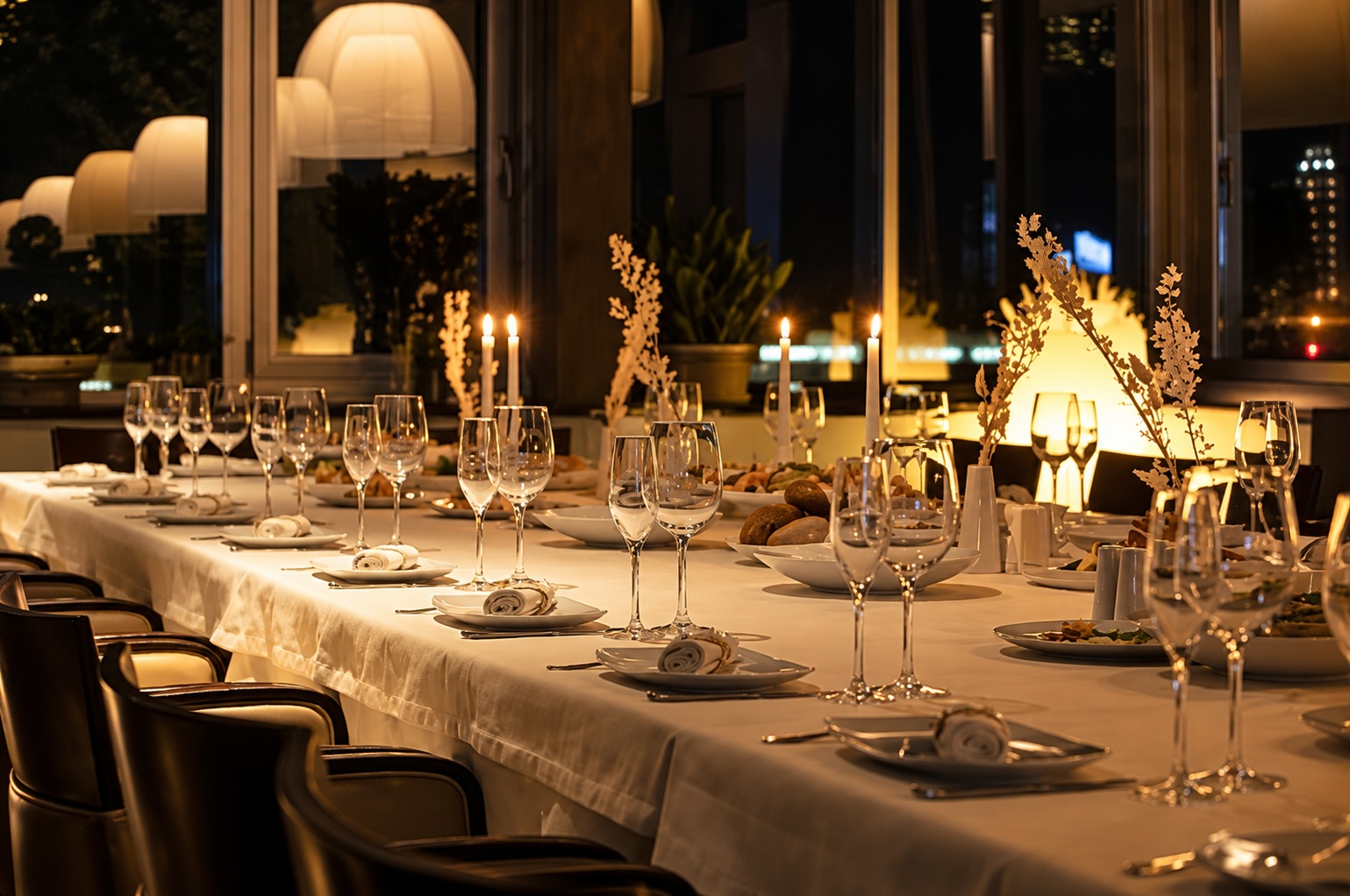 Table dressée pour un dîner privé, verres à vin et bougies allumées, ambiance tamisée avec vue sur la ville.